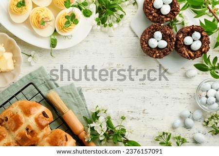 Easter brunch or breakfast. Easter chocolate nest cake with chocolate candy eggs, traditional hot cross buns and deviled eggs with bouquets of blooming apple trees. Spring Easter holiday food concept.