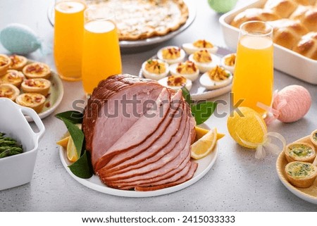 Easter brunch on large table with spiral sliced ham, quiche, deviled eggs and hot cross buns with Easter decor