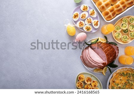 Easter brunch on large table with spiral sliced ham, quiche, deviled eggs and hot cross buns with Easter decor with copy space