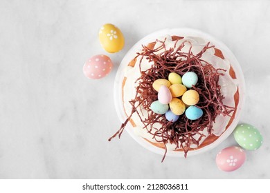 Easter Bundt Cake With Chocolate Nest Of Colorful Candy Eggs. Overhead View On A White Marble Background.