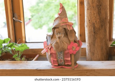 Easter bunny doll in a hat on a wooden shelf in front of the window.