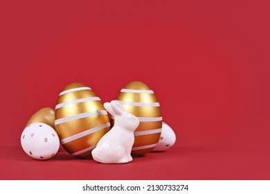 Easter bunny figure and golden and white easter eggs with stripes and dots on dark red background with copy space - Powered by Shutterstock