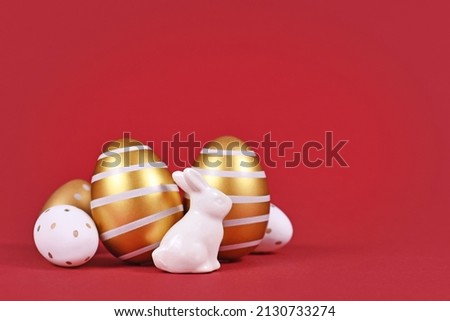 Easter bunny figure and golden and white easter eggs with stripes and dots on dark red background with copy space