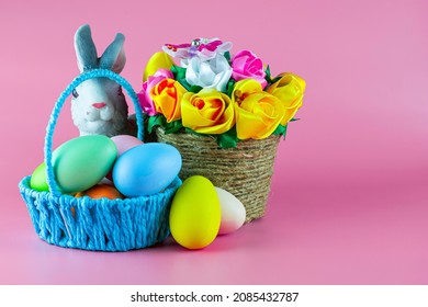 easter bunny and painted Easter eggs in a basket next to a basket of flowers on a pink background. copyscape. High quality photo