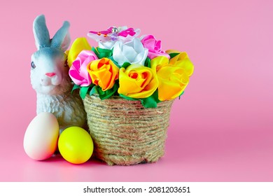 easter bunny and painted easter eggs next to a basket of flowers on a pink background copyscape. High quality photo