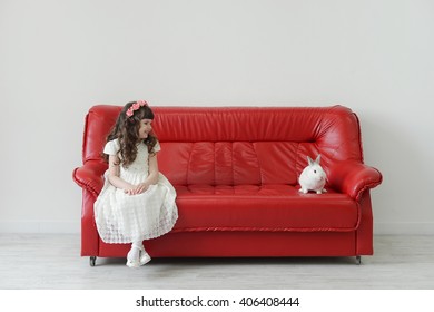 Easter Bunny Small And Cute With A Little Girl In A White Dress On The Red Couch In A Textural White Studio