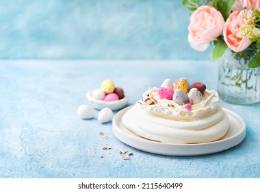 Easter cake Meringue nest cake Pavlova with colorful chocolate eggs, buttercream frosting, light blue background with copy space. Selective focus. Close up. Easter Spring love feast concept.