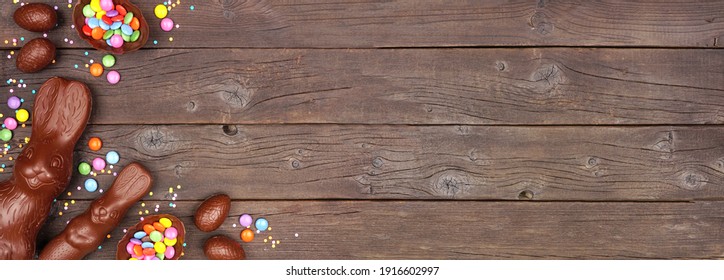 Easter Candy And Chocolate Bunnies And Eggs. Corner Border Against A Rustic Dark Wood Banner Background. Copy Space.