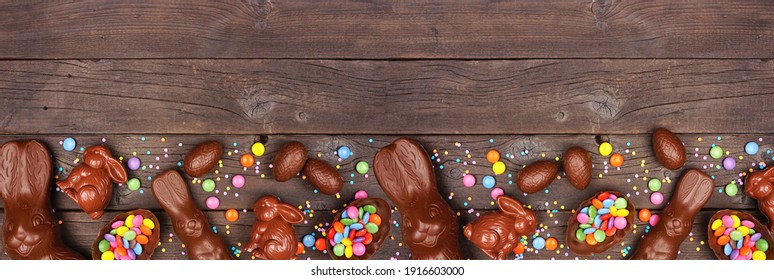 Easter Candy And Chocolate Bunnies And Eggs. Bottom Border Against A Rustic Dark Wood Banner Background. Copy Space.