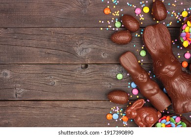 Easter Candy And Chocolate Bunnies And Eggs. Side Border Against A Rustic Dark Wood Banner Background. Copy Space.