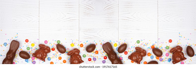 Easter Candy, Chocolate Bunnies And Eggs. Overhead View Bottom Border Against A White Wood Banner Background. Copy Space.