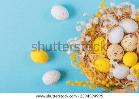 Easter candy chocolate eggs and almond sweets lying in a bird's nest decorated with flowers and feathers on a blue background. Happy Easter concept.
