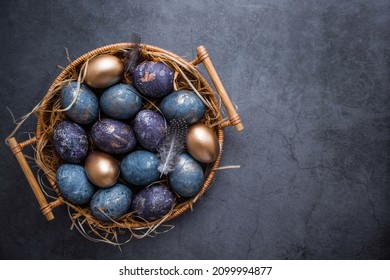 Easter card with a copy of the place for the text. Purple, blue and golden eggs in a basket on a dark background. The purple hue trend of 2022 is very peri. Natural dye karkade tea. Top view.