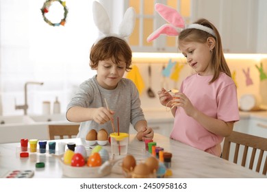 Easter celebration. Cute children with bunny ears painting eggs at white marble table in kitchen - Powered by Shutterstock