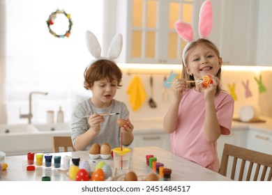 Easter celebration. Cute children with bunny ears painting eggs at white marble table in kitchen - Powered by Shutterstock