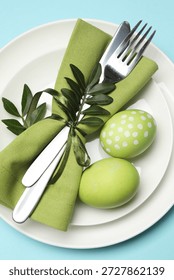 Easter celebration. Festive table setting with green leaves and painted eggs on light blue background, top view