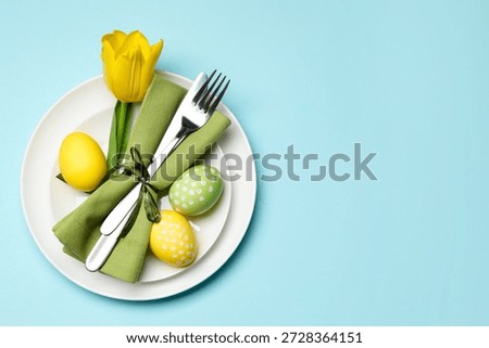 Easter celebration. Festive table setting with tulip flower and painted eggs on light blue background, top view. Space for text