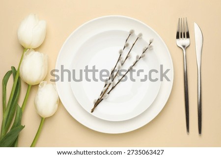 Easter celebration. Festive table setting with tulip flowers, willow branches and cutlery on beige background, flat lay
