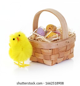 An Easter Chick And Candy Eggs In A Basket With Straw On White