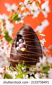 Easter chocolate egg with spring flowers on vibrant orange background