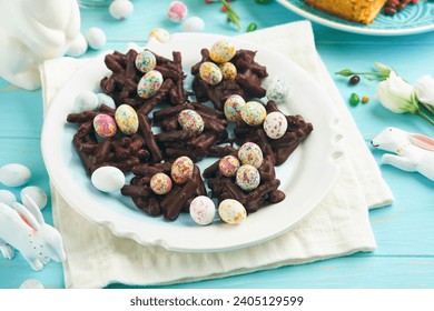 Easter chocolate nest cake with mini chocolate candy eggs with blossoming cherry or apple flowers on blue background table. Creative recipe for Easter table with holiday decorations. Top view.