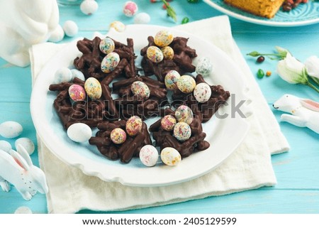 Easter chocolate nest cake with mini chocolate candy eggs with blossoming cherry or apple flowers on blue background table. Creative recipe for Easter table with holiday decorations. Top view.