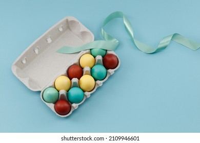 Easter colorful eggs in a dozen egg carton with ribbon on blue background 