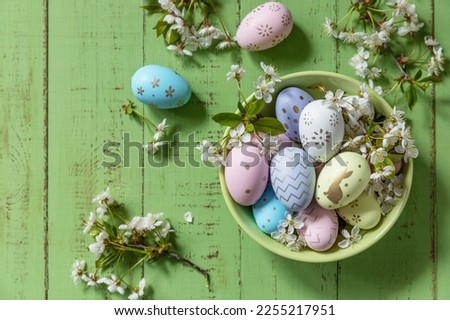 Easter composition. Branches of a blooming apple tree, handmade Easter colorful eggs on a pastel rustic wooden table. Happy Easter Holidays. View from above.