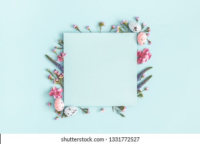 Easter composition. Easter eggs, flowers, paper blank on pastel blue background. Flat lay, top view, copy space.