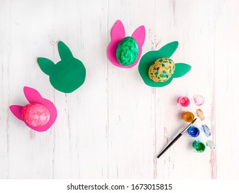 Easter composition with eggs painted by a child. Easter eggs on paper rabbits and multi-colored paints with a brush. Copy space for text, top view