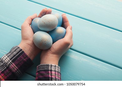 Easter composition. Female hands holding blue colored eggs with golden sprinkles on rustic wooden table. Spring holiday background, copy space