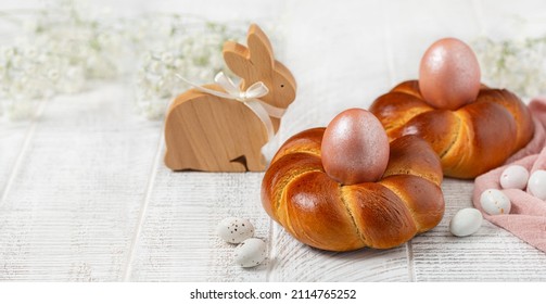 Easter composition with italian style homemade braid bread, pink metallic colored eggs and wooden easter bunny. White flowers. White wooden background. Selective focus, bunner size. - Powered by Shutterstock