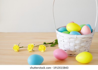 Easter composition on the table. Colored eggs with basket and small flowers on wooden table with white background and copy space for text.