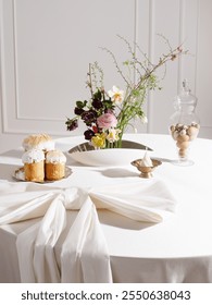 Easter composition on the table with flowers in kenzan, Easter cakes, eggs and a candle. Bright festive table
