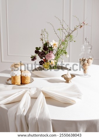Easter composition on the table with flowers in kenzan, Easter cakes, eggs and a candle. Bright festive table