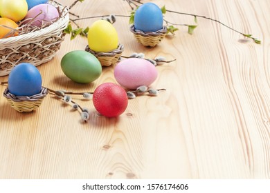 Easter composition - several colored eggs in a basket and on a light wooden table with willow twigs, place for text, copy space