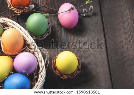 Easter composition - several colored eggs in a basket and on a dark wooden table with willow twigs, place for text, copy space