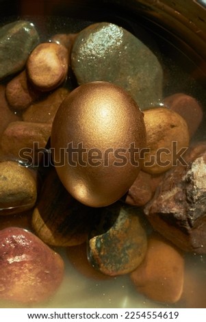Easter concept and craft decorations, a golden egg on small rocks and water in the background. Zenithal view