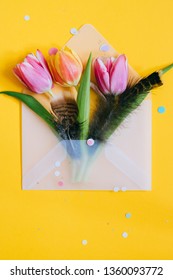 Easter Confetti S And Open Matte Transparent Envelope With Multicolored Tulips An Quail Eggs On Yellow Background.