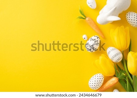 Easter creative display: Top view of simplistic colored eggs, delightful hare figurine, carrot treats, and fresh tulips on bright yellow canvas, with space reserved for text or adverts