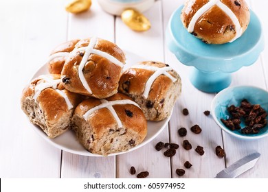 Easter cross-buns and sultanas on a white plate on white wooden background close up