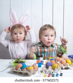Easter Day. Moden Family Preparing For Easter. Son Painting Eggs On Wooden Background. Having Fun On Easter Egg Hunt. Cute Child Boy And Girl Wearing Bunny Ears. Colorful Eggs In Basket.