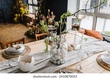 Easter decor closeup. Setting table for Easter dinner with candles, ceramic plates with easter eggs in nest, Easter bunny made of linen napkin. Holidays celebration concept. Side view. Set up.