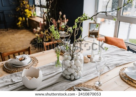Easter decor closeup. Setting table for Easter dinner with candles, ceramic plates with easter eggs in nest, Easter bunny made of linen napkin. Holidays celebration concept. Side view. Set up.