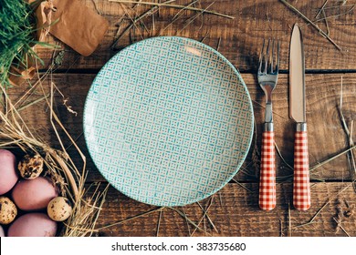 Easter Dinner. Top View Of Easter Eggs In Bowl And Plate With Fork And Knife Lying On Wooden Rustic Table With Hay