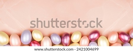 Easter Egg bottom border over a soft pink stone banner background. Shiny, pink, purple and yellow eggs. Copy space.
