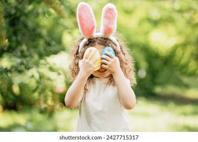 Easter egg hunt. Girl child Wearing Bunny Ears Running To Pick Up Egg In Garden. Easter tradition. Baby with basket full of colorful eggs. - Powered by Shutterstock