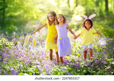 Cacería de huevos en Pascua. Grupo de niños buscando huevos coloridos. Los niños usan orejas de conejo. Muchacho y chica con cesta de huevos durante las vacaciones de primavera en un parque soleado. Prado de flores de primavera.