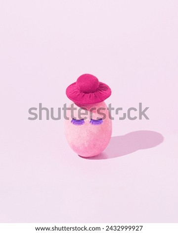 Easter egg pastel pink colored with hat and shiny purple eyelashes.  Minimal creative food concept. Surreal egg design. Front view. Copy space.