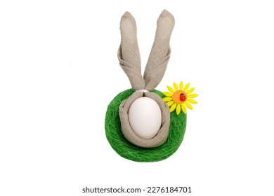 Easter egg with rabbit ears, in a green nest, from grass with a yellow flower.